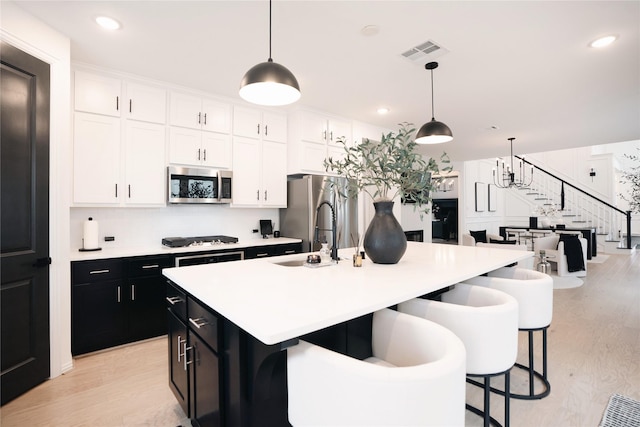 kitchen featuring decorative light fixtures, a kitchen island with sink, white cabinetry, appliances with stainless steel finishes, and sink