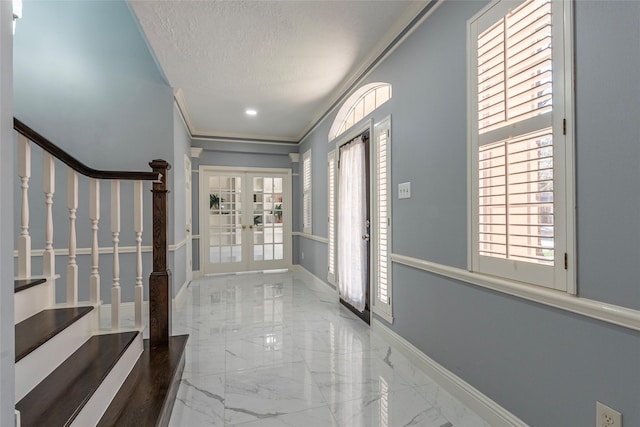 entrance foyer with a textured ceiling, french doors, ornamental molding, and a wealth of natural light