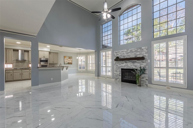 unfurnished living room with a high ceiling, ceiling fan, and a stone fireplace