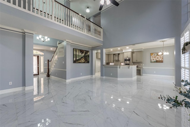 unfurnished living room featuring a towering ceiling and ceiling fan with notable chandelier