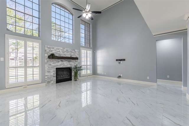 unfurnished living room with a high ceiling, ceiling fan, and a stone fireplace