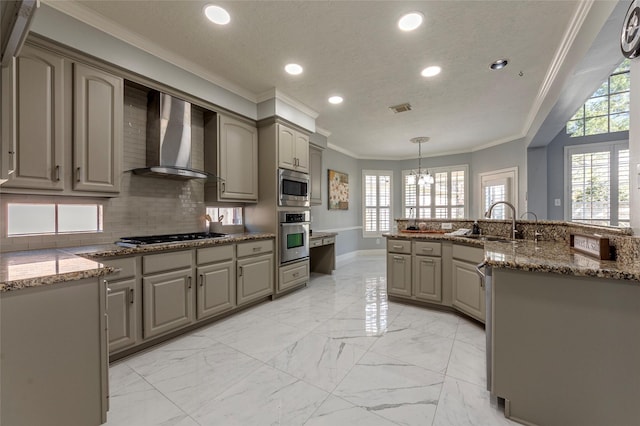 kitchen featuring decorative light fixtures, wall chimney range hood, decorative backsplash, appliances with stainless steel finishes, and sink