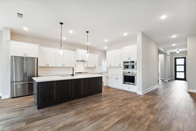 kitchen with pendant lighting, dark hardwood / wood-style floors, a kitchen island with sink, white cabinetry, and appliances with stainless steel finishes