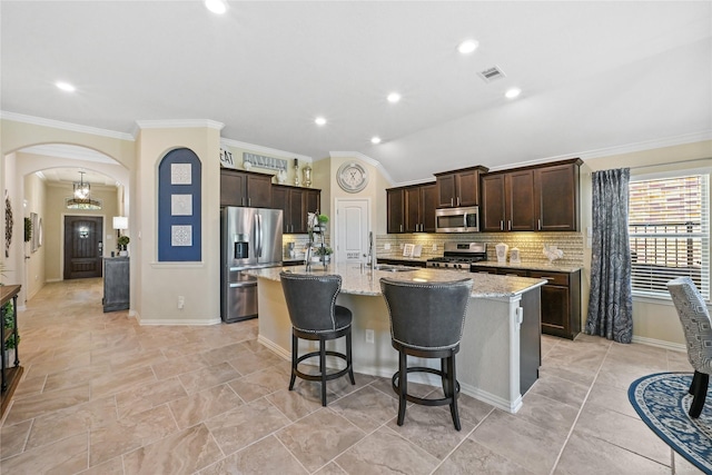 kitchen with stainless steel appliances, vaulted ceiling, light stone counters, a kitchen bar, and a center island with sink