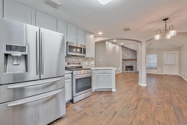 kitchen featuring appliances with stainless steel finishes, tasteful backsplash, white cabinets, decorative light fixtures, and light hardwood / wood-style flooring