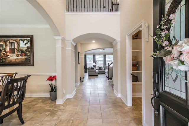 tiled entryway featuring ceiling fan, ornamental molding, and ornate columns