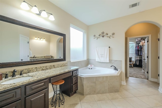 bathroom featuring a relaxing tiled tub, tile patterned floors, and vanity