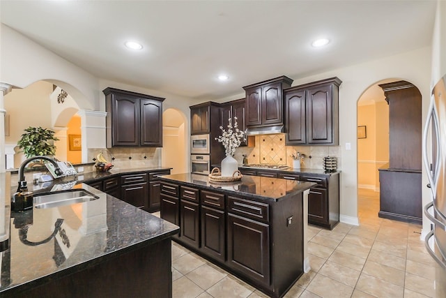 kitchen featuring stainless steel appliances, a center island, sink, dark brown cabinets, and tasteful backsplash