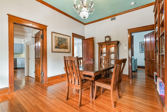 dining area with an inviting chandelier, light wood-type flooring, and crown molding