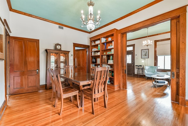 dining room featuring light wood-type flooring, crown molding, and a notable chandelier