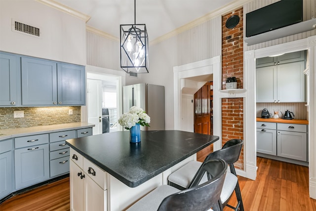 kitchen with ornamental molding, light hardwood / wood-style flooring, backsplash, stainless steel fridge, and a kitchen island