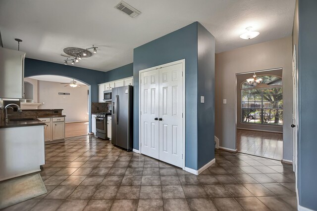 kitchen with stainless steel appliances, white cabinets, ceiling fan with notable chandelier, and sink