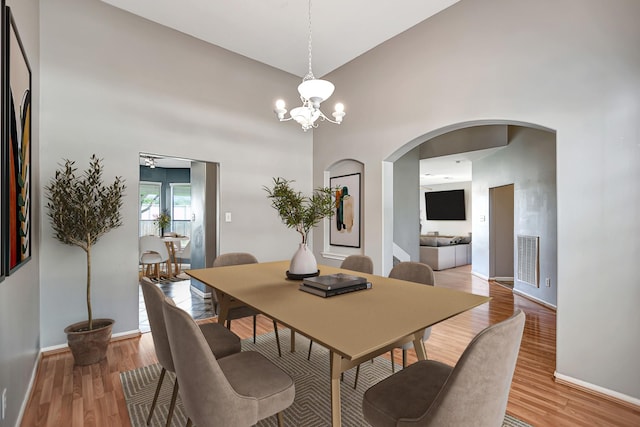 dining area with a high ceiling, light hardwood / wood-style flooring, and ceiling fan with notable chandelier