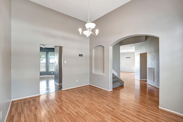 empty room with ceiling fan with notable chandelier and light hardwood / wood-style floors