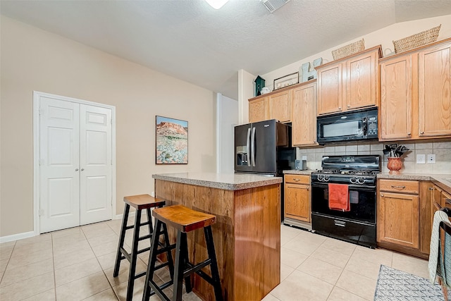 kitchen featuring a center island, light tile patterned floors, black appliances, backsplash, and a breakfast bar area