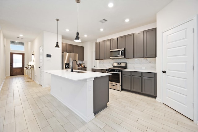 kitchen featuring decorative light fixtures, stainless steel appliances, a center island with sink, decorative backsplash, and sink