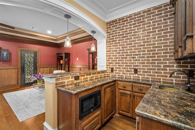 kitchen featuring black microwave, hanging light fixtures, kitchen peninsula, and dark stone counters