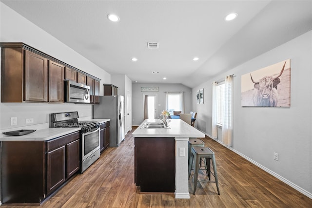 kitchen with vaulted ceiling, a center island with sink, dark hardwood / wood-style flooring, appliances with stainless steel finishes, and a kitchen breakfast bar