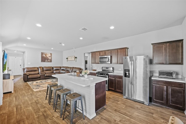 kitchen featuring light hardwood / wood-style flooring, a kitchen island, a breakfast bar area, appliances with stainless steel finishes, and dark brown cabinets