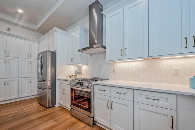 kitchen with stainless steel appliances, wall chimney range hood, tasteful backsplash, light wood-type flooring, and white cabinetry