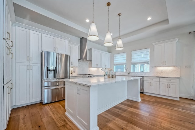 kitchen featuring wall chimney exhaust hood, white cabinets, a center island, and appliances with stainless steel finishes