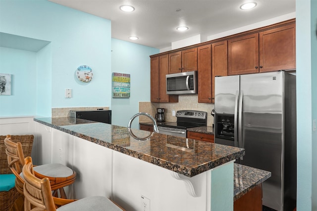 kitchen with a kitchen bar, appliances with stainless steel finishes, kitchen peninsula, and dark stone counters