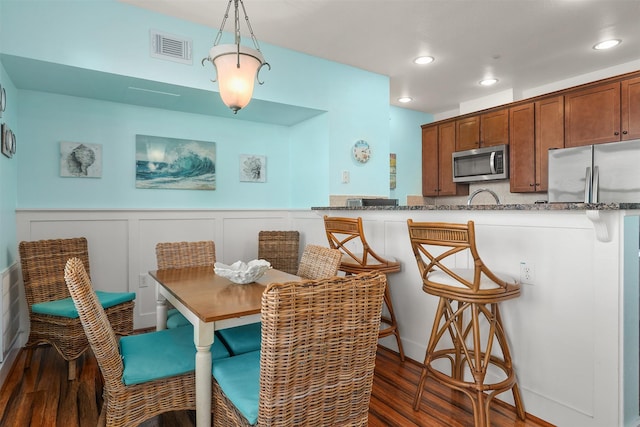 kitchen with appliances with stainless steel finishes, dark hardwood / wood-style flooring, dark stone counters, a kitchen breakfast bar, and hanging light fixtures