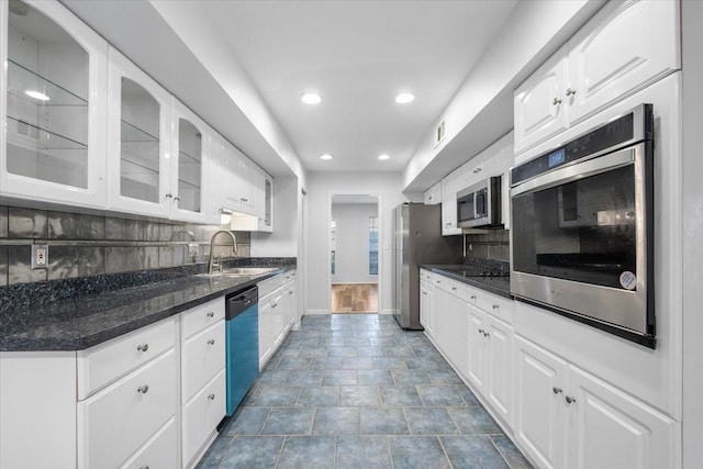 kitchen featuring white cabinets, stainless steel appliances, dark stone counters, decorative backsplash, and sink