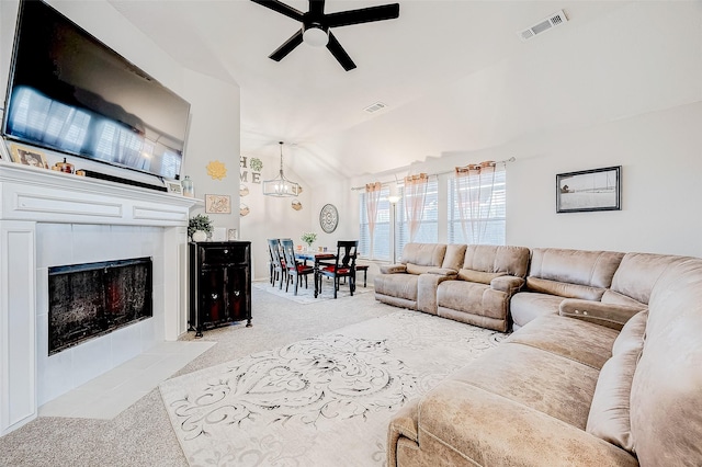 living room with ceiling fan with notable chandelier, a tiled fireplace, vaulted ceiling, and light colored carpet