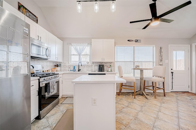 kitchen featuring a center island, hanging light fixtures, lofted ceiling, white cabinetry, and appliances with stainless steel finishes