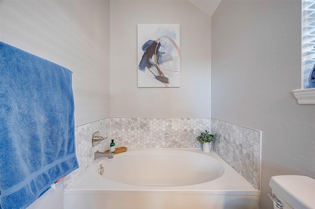 bathroom with toilet, a tub to relax in, and lofted ceiling