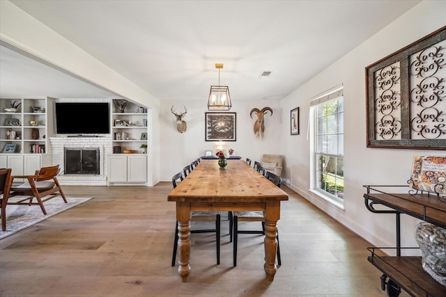 dining space with a fireplace, light wood-type flooring, and built in features