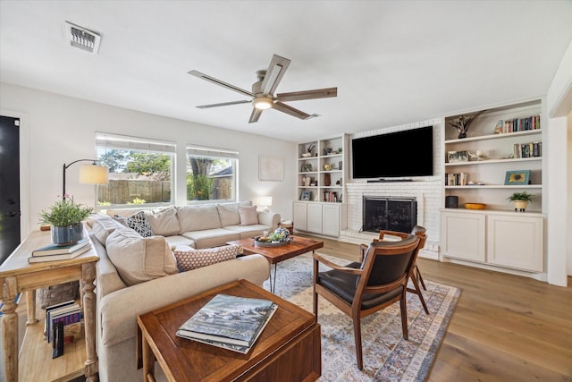 living room featuring a brick fireplace, hardwood / wood-style flooring, built in features, and ceiling fan