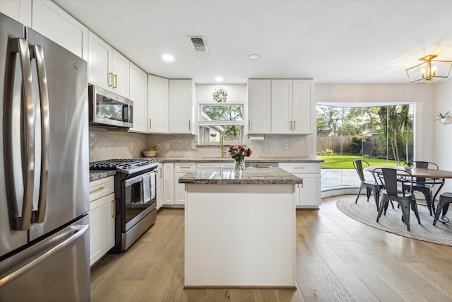 kitchen with stainless steel appliances, white cabinets, light stone counters, and a center island