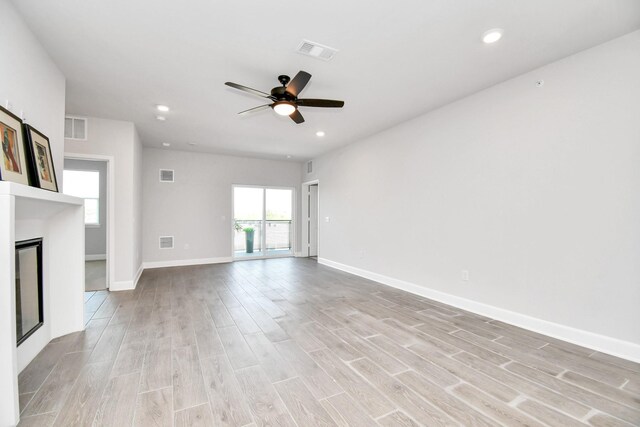 unfurnished living room with light wood-style floors, plenty of natural light, visible vents, and a glass covered fireplace