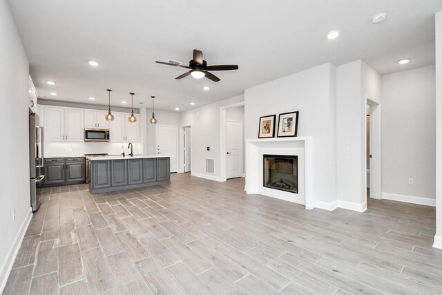 kitchen featuring a glass covered fireplace, light wood-style flooring, appliances with stainless steel finishes, open floor plan, and gray cabinetry