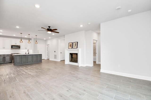 unfurnished living room featuring a fireplace, recessed lighting, a ceiling fan, light wood-type flooring, and baseboards