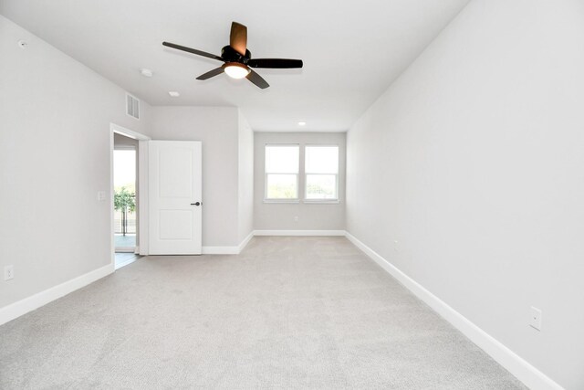 spare room with a ceiling fan, light colored carpet, visible vents, and baseboards