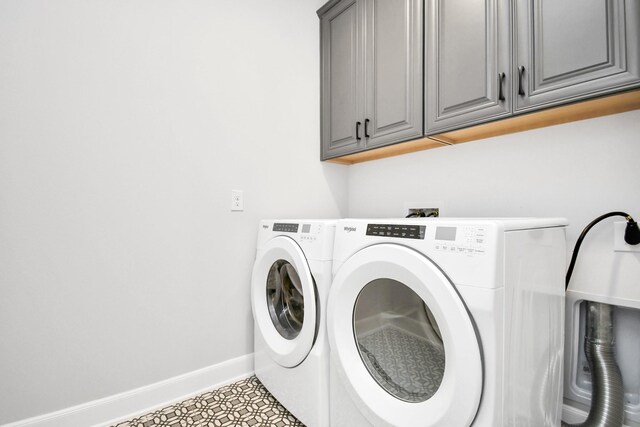 clothes washing area featuring washing machine and dryer, cabinet space, and baseboards