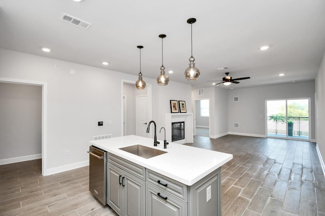 kitchen with visible vents, a glass covered fireplace, a sink, wood tiled floor, and a wealth of natural light