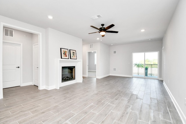 unfurnished living room with light wood-type flooring, visible vents, and a glass covered fireplace