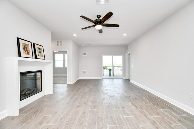 unfurnished living room with a wealth of natural light, light wood-style flooring, a glass covered fireplace, and visible vents