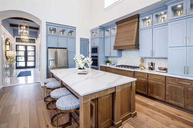 kitchen featuring stainless steel appliances, a center island, light wood-type flooring, custom exhaust hood, and light stone countertops