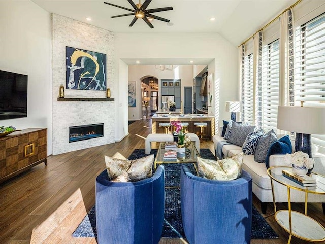 living room with lofted ceiling, ceiling fan, dark hardwood / wood-style floors, and a stone fireplace