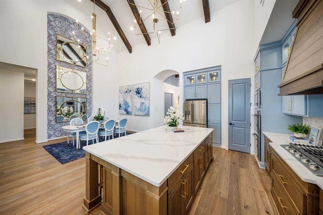 kitchen with a chandelier, a center island, a towering ceiling, appliances with stainless steel finishes, and beamed ceiling