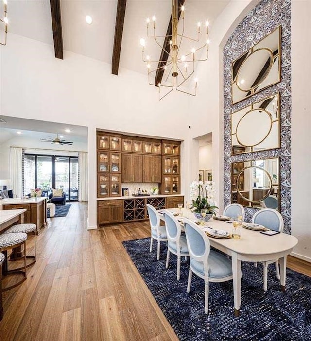 dining room with beamed ceiling, high vaulted ceiling, ceiling fan with notable chandelier, and wood-type flooring