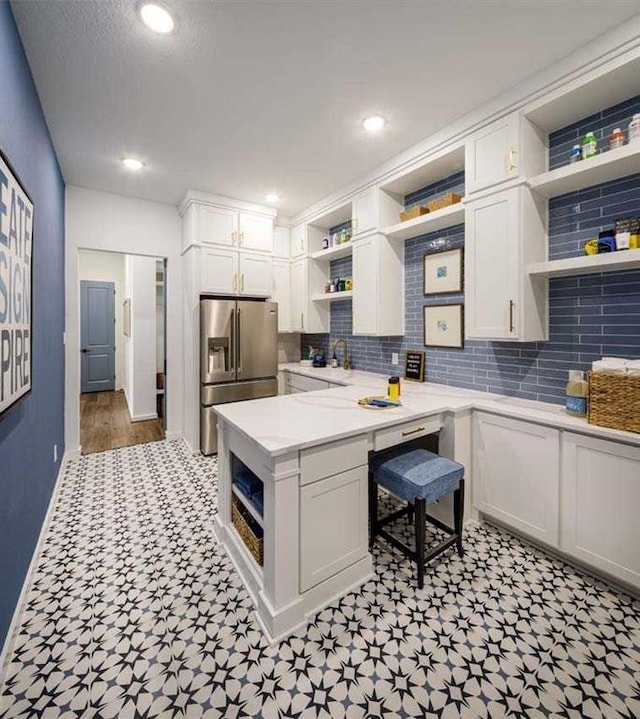 kitchen featuring kitchen peninsula, tasteful backsplash, white cabinetry, high end refrigerator, and sink