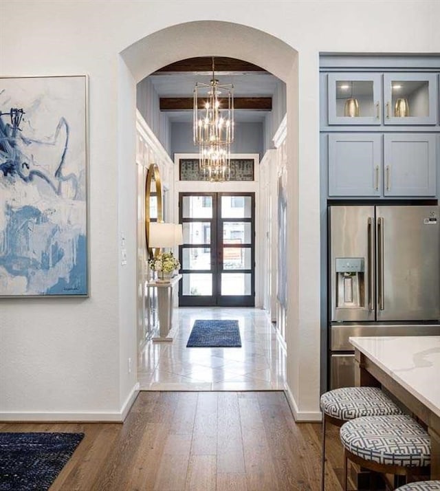 foyer featuring french doors, dark wood-type flooring, a notable chandelier, and beam ceiling