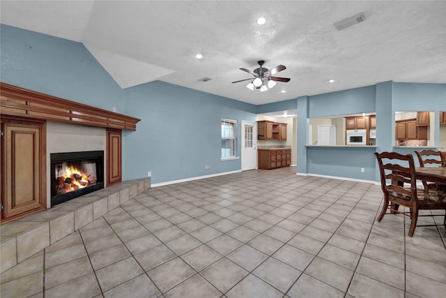 unfurnished living room featuring ceiling fan, a tiled fireplace, light tile patterned flooring, lofted ceiling, and a textured ceiling