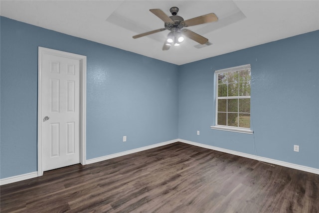 empty room with ceiling fan, dark hardwood / wood-style flooring, and a raised ceiling